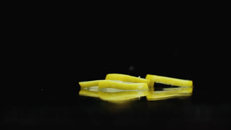 Slow-motion.-Sliced-​​lemon-rings-fall-with-splashes-of-water-on-the-glass-on-a-dark-background.-Cut-into-slices